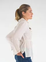 Blusa blanca de broderie de manga larga, con cuello camisero, cierre frontal de botones y cordón ajustable en la cintura.