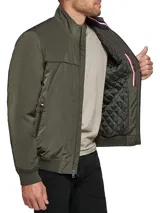Campera bomber verde militar de poliéster, con cuello mao, cierre frontal con cremallera, dos bolsillos laterales con cremallera, puños y ruedo elásticos. Logo de Tommy Hilfiger bordado en el pecho.