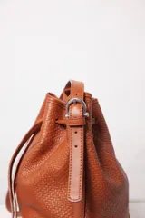 Cartera tipo botellero color marrón con efecto trenzado, tamaño mediano, cierre con frunce, correa ajustable con hebilla para usar al hombro o cruzada, doble bolsillo interior (uno con cierre).