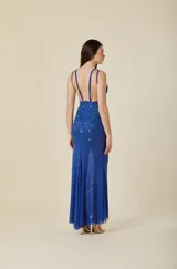 Vestido largo de tul elastizado color azul, con escote en V y tirantes finos. Presenta apliques bordados a mano y detalles de canutillos al tono en el torso, con una falda de caída suave y fluida.