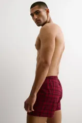 Pack de dos calzoncillos tipo boxer en tejido suave, con cintura elástica y bragueta de botones. Uno de ellos presenta un patrón a cuadros pequeños en tonos rojo y blanco, mientras que el otro cuenta con un diseño de cuadros tipo tartán en tonos rojo y negro.