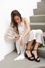 Sandalias de tacón alto con plataforma, confeccionadas en cuero con acabado brillante tipo charol, color negro. Poseen tira delantera ancha, tira ajustable al tobillo con hebilla metálica dorada, y taco ancho.