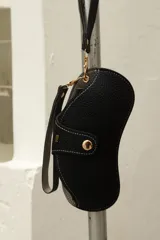 Funda para lentes de cuero sintético negro con cierre de botón a presión y correa de mano.