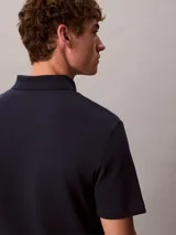 Chomba de manga corta Calvin Klein confeccionada en algodón interlock, con cuello clásico y cierre frontal de botones. Presenta un diseño liso en color azul marino con el logo de la marca sutilmente bordado en el pecho.
