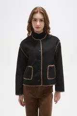 Chaqueta negra de poliéster con cuello a la base, cierre frontal con botones y dos bolsillos delanteros. Presenta detalles de bordado decorativo en color marrón en los bordes, cuello, puños y bolsillos.