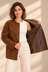 Camisa de cuero color marrón, de corte recto y largo medio, con cuello redondo a la base, cierre frontal con broches metálicos y bolsillos aplicados en los laterales.