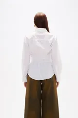 Camisa blanca de poliéster con cuello clásico, manga larga con puños anchos y detalle de frunces en la cintura que crea un efecto entallado.