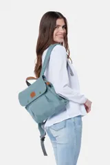 Mochila de lona estilo vintage con solapa frontal, bolsillos laterales y correas ajustables. Presenta detalles en cuero sintético y un parche decorativo en la parte superior.