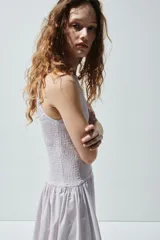 Vestido midi sin mangas confeccionado en sirsaca de algodón color lila, con cuerpo ajustado de punto smock, escote redondo y falda amplia con vuelo y costura fruncida en la cadera.