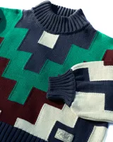 Sweater de cuello alto tejido con diseño geométrico en zigzag multicolor, incluyendo tonos azul marino, verde, bordó y crema. Presenta puños y ruedo acanalados.