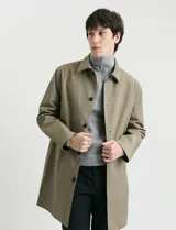 Gabardina clásica de corte recto, color beige, con cuello camisero, cierre frontal de botones y bolsillos laterales. Confeccionada en tejido técnico repelente al agua y al viento.