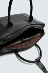 Maletín de cuero negro con acabado abatanado, cierre de cremallera, doble asa de mano, asa de hombro ajustable y extraíble, bolsillo interno para dispositivos electrónicos de hasta 13 pulgadas y detalle de candado. Marca Mango.