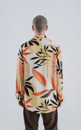 Camisa de manga larga con cuello y botones frontales, confeccionada en rayón con un estampado de hojas tropicales en tonos beige, naranja, negro y verde oliva.