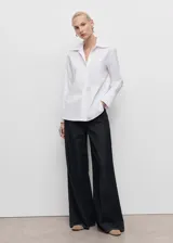 Camisa de corte recto en color blanco, con cuello camisero de solapas amplias, cierre frontal oculto con botones y mangas largas con puños abotonados.