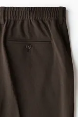 Pantalón de corte relajado color marrón, con cierre de botón, cintura con elástico y cordón interno, bolsillos laterales al bies y bolsillos traseros ribeteados con botón.