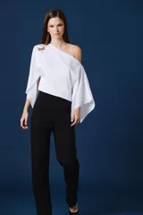 Blusa blanca de un solo hombro con mangas amplias y fluidas. Presenta un diseño asimétrico con un broche decorativo en forma de libélula en el hombro derecho.