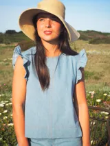 Blusa sin mangas de denim liviano color celeste, con diseño recto, costuras pespunteadas en contraste y volados decorativos en los hombros.