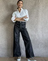 Pantalón de jean negro de corte recto y tiro alto, con costuras a la vista en color blanco que resaltan su diseño. Presenta un estilo moderno con bolsillos laterales y cierre frontal.