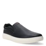 Zapato tipo slip-on de hombre, color negro, con capellada de cuero texturizado y elásticos laterales para un ajuste fácil. Presenta una suela gruesa de goma color blanco crema y un detalle de parche de cuero marrón en la lengüeta y el talón.