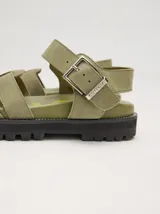 Sandalias de cuero marrón con tiras entrecruzadas, suela de goma negra con pespuntes blancos y hebilla lateral.