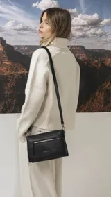 Bandolera de tamaño mediano en color gris, confeccionada en símil cuero con textura granulada. Presenta un bolsillo frontal con cierre, herrajes metálicos oscuros y correa ajustable y desmontable.