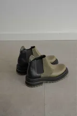 Botas tipo Chelsea con diseño bicolor en tonos negro y verde oliva. Presentan paneles laterales elásticos, suela track robusta y tirador trasero.