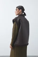 Chaleco de cuero sintético negro con interior y detalles de corderito en cuello, sisas y ruedo. Presenta cierre frontal completo y diseño holgado.