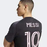 Camiseta de fútbol Adidas alternativa del Inter Miami CF, color negro y gris oscuro con diseño dividido verticalmente. Presenta detalles en rosa, incluyendo el logo de Adidas, el escudo del club y un gráfico central que simula un ancla con corona.