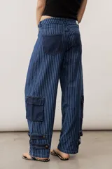 Jean de corte cargo y estilo holgado, con diseño de rayas verticales en tonos de azul. Presenta bolsillos laterales con solapa y detalles de tiras ajustables con hebillas en los tobillos.