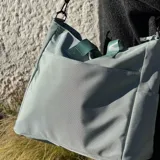 Bolso tipo tote y shopper de color negro, confeccionado en poliéster con amplio espacio interior, doble asa de mano y correa larga ajustable para llevar al hombro o cruzado.