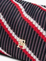 Cartera tipo hobo de Tommy Hilfiger con diseño de rayas diagonales en azul marino, rojo y blanco. Presenta un asa superior fija, una correa ajustable extraíble, cierre superior y el logo metálico TH en la parte frontal.
