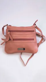 Bandolera color marrón con apertura superior de cierre metálico y dos bolsillos frontales con cierre. Incluye correa larga regulable y placa metálica con el logo de la marca.