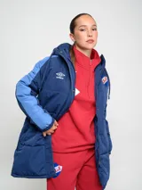Parka larga de abrigo Umbro del Club Nacional de Football, color rojo con detalles en naranja en las mangas. Cuenta con capucha, cierre frontal con botones a presión y escudo del club bordado en el pecho.