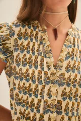 Vestido corto de algodón con estampado floral en tonos amarillos y azules. Presenta un diseño con volados en las mangas y en el ruedo, con detalles de ribetes en color azul y una textura con hilos metalizados.