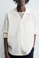 Camisa de calce relajado confeccionada en tejido ligero de algodón con textura. Presenta cuello bowling, manga corta, un bolsillo de parche en el pecho y cierre frontal con botones. El bajo cuenta con aberturas laterales.