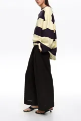 Pantalón tobillero de corte campana color negro, confeccionado en mezcla de algodón y viscosa. Presenta cierre frontal con botón, tiro medio, bolsillos diagonales, cinturilla elástica y vuelta en el bajo de la pierna.