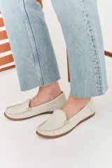 Mocasines de cuero color dorado con acabado texturizado, diseño clásico de punta redondeada y costuras visibles en el empeine. Cuentan con suela plana y flexible.