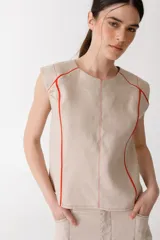 Blusa sin mangas color beige, confeccionada en lino, con costuras y pespuntes en hilo rojo contrastante que definen el canesú y los laterales.
