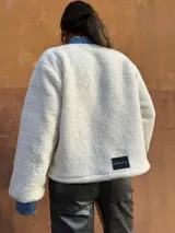 Chaqueta color crema de corderito con detalles en jean azul en cuello, solapa, bolsillos y puños.