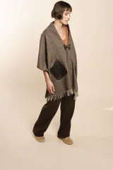 Chal de lana fina sin teñir con diseño de cuadros sutiles, cierre frontal con alamar y bolsillos de cuero metalizado. Presenta terminaciones con flecos en el ruedo y un calce estructurado en los hombros.