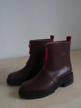 Botas de cuero color marrón con suela track negra y cierre frontal con cremallera roja.