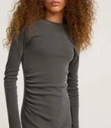 Vestido midi gris confeccionado en rib de algodón y elastano. Posee cuello redondo, manga larga y drapeado lateral con abertura en la parte inferior.