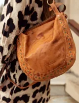 Cartera de cuero roja con tachas plateadas en el borde inferior, doble asa de cuero y cierre superior.