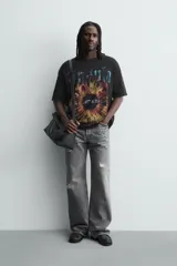 Camiseta de punto negro con efecto lavado, corte relaxed fit y cuello redondo. Presenta un estampado frontal con tipografía gótica en azul y una imagen circular que simula un iris en tonos rojizos y amarillos.