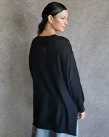 Buzo de tejido de punto en color gris claro, con cuello redondo, mangas largas con hombros caídos y diseño de corte asimétrico con la parte trasera más larga que la delantera.