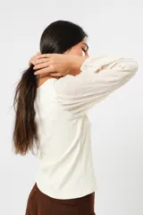 Blusa color manteca de cuello redondo y mangas largas abullonadas con puños elásticos.