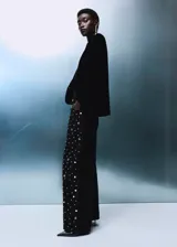 Jeans rectos de tiro medio en tejido de algodón vaquero color negro, con diseño de cinco bolsillos, trabillas para cinturón y cierre frontal con botón y cremallera. Presenta aplicaciones de tachuelas brillantes a lo largo de las piernas.