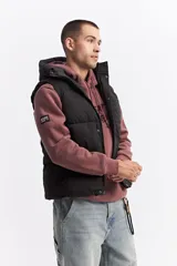 Chaleco puffer acolchado color azul marino, con capucha fija, cierre frontal con solapa de botones a presión y bolsillos laterales con cierre. Presenta un parche con el logo de la marca en el pecho.