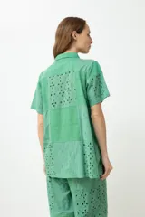 Camisa verde con cuello clásico, manga corta y cierre frontal con botones. Presenta diseño patchwork con detalles de broderie y calados.