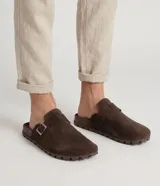 Zuecos mule de gamuza marrón, con diseño cerrado en la parte delantera, tira ajustable con hebilla metálica lateral y suela dentada de goma.